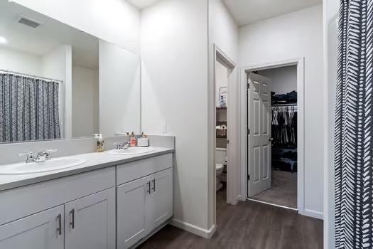 full bath with double vanity, toilet, a sink, and wood finished floors