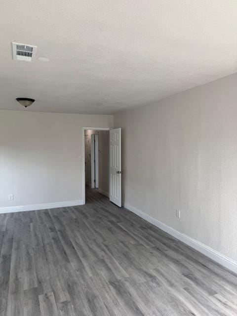 unfurnished room featuring dark wood-style floors, visible vents, a textured ceiling, and baseboards