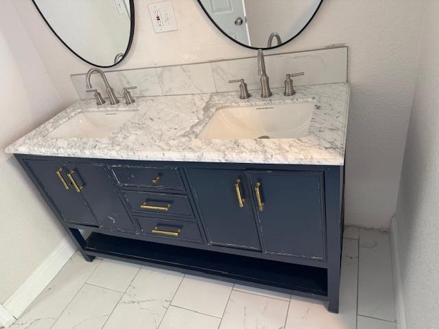 full bath with marble finish floor, double vanity, and a sink