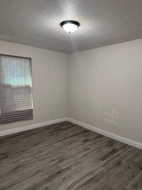 empty room with baseboards, dark wood finished floors, and a textured ceiling