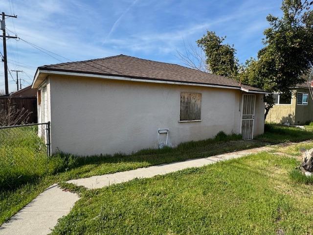 view of side of property featuring a yard, roof with shingles, fence, and stucco siding