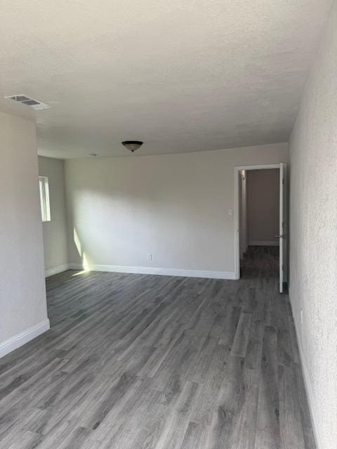 unfurnished room with visible vents, dark wood finished floors, a textured ceiling, and baseboards