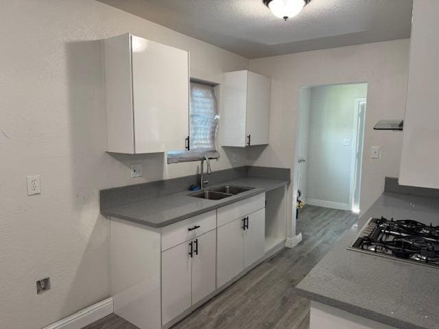 kitchen with dark countertops, dark wood-style floors, stainless steel gas stovetop, white cabinetry, and a sink