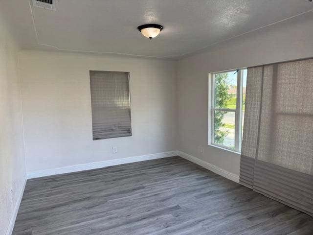 unfurnished room with dark wood-style flooring, visible vents, and baseboards