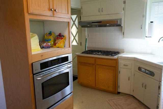 kitchen featuring tile countertops, backsplash, stainless steel appliances, and ventilation hood