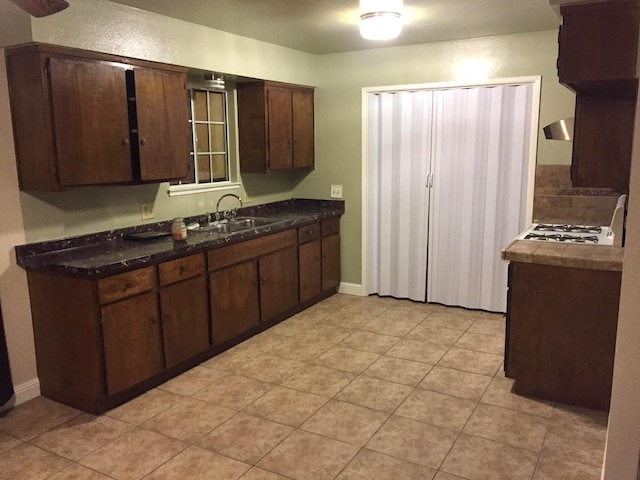 kitchen featuring dark countertops, dark brown cabinetry, baseboards, and a sink