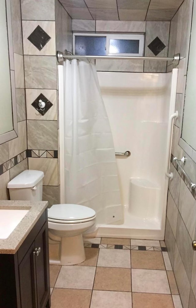 full bathroom with tile walls, toilet, a shower stall, vanity, and tile patterned floors