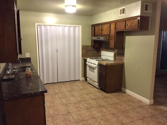 kitchen with white gas stove, dark countertops, visible vents, and under cabinet range hood