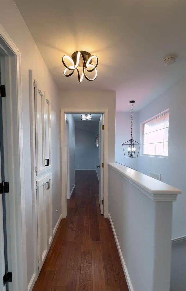 hallway with baseboards, visible vents, a chandelier, and dark wood finished floors