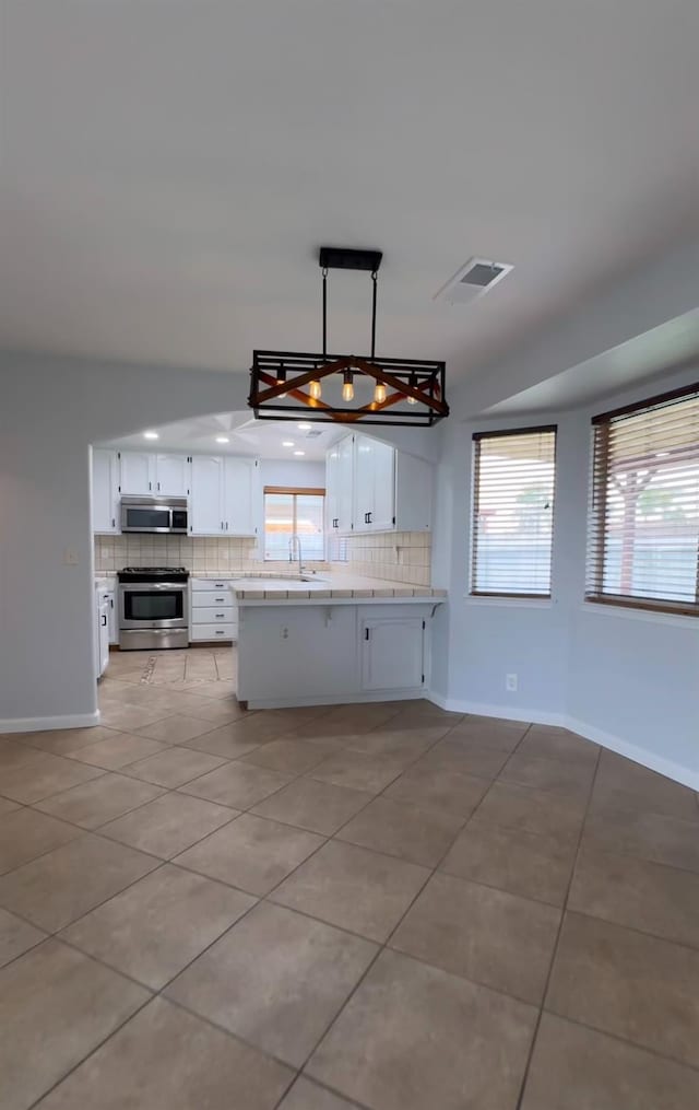 kitchen with appliances with stainless steel finishes, white cabinetry, hanging light fixtures, and visible vents