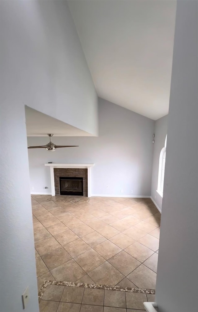 unfurnished living room with light tile patterned floors, baseboards, ceiling fan, a fireplace, and high vaulted ceiling