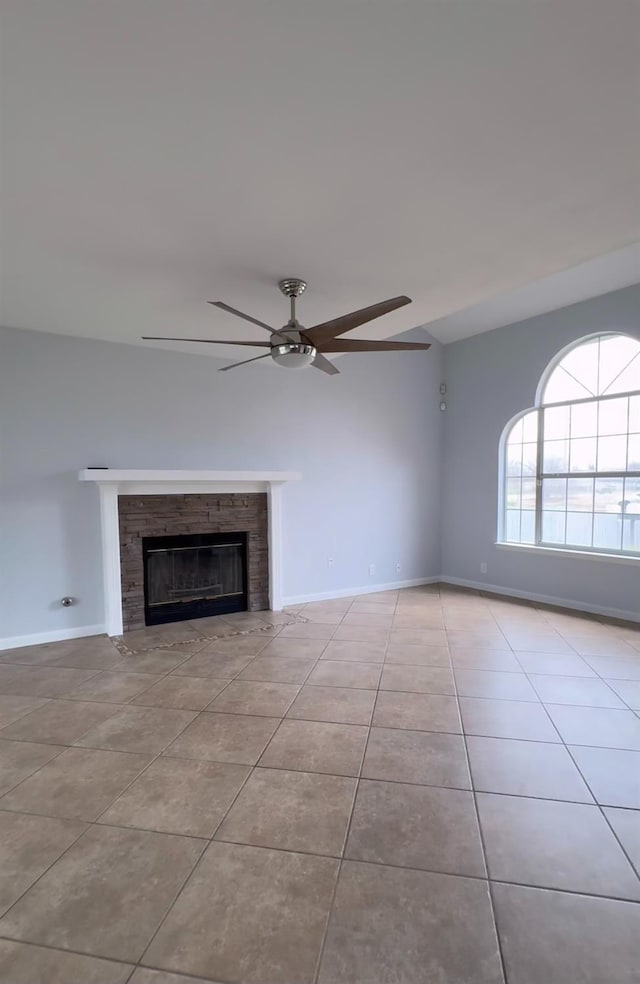 unfurnished living room featuring lofted ceiling, light tile patterned flooring, a ceiling fan, baseboards, and a glass covered fireplace