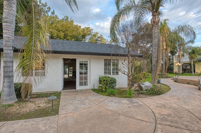 entrance to property featuring roof with shingles, french doors, and stucco siding