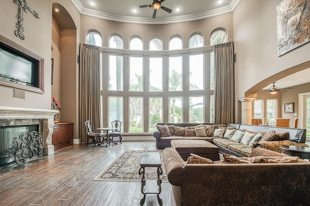 living area with arched walkways, a high ceiling, wood finished floors, a high end fireplace, and a ceiling fan