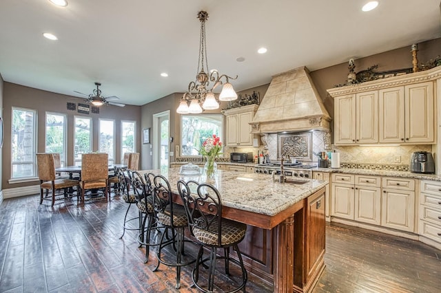 kitchen with dark wood-style floors, cream cabinetry, custom exhaust hood, tasteful backsplash, and light stone countertops