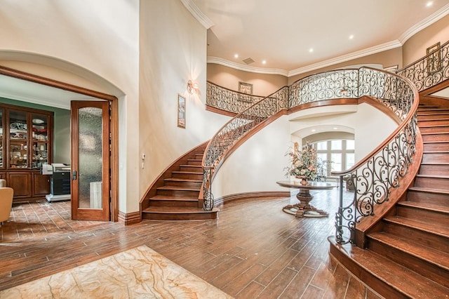 entryway with baseboards, a towering ceiling, stairway, wood finished floors, and crown molding