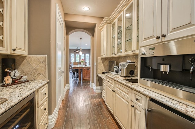 kitchen with arched walkways, dark wood-type flooring, cream cabinets, and decorative backsplash