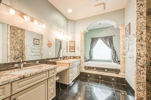 bathroom featuring decorative columns, two vanities, granite finish floor, a sink, and a bath