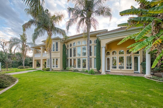 rear view of house featuring a lawn, a balcony, and stucco siding