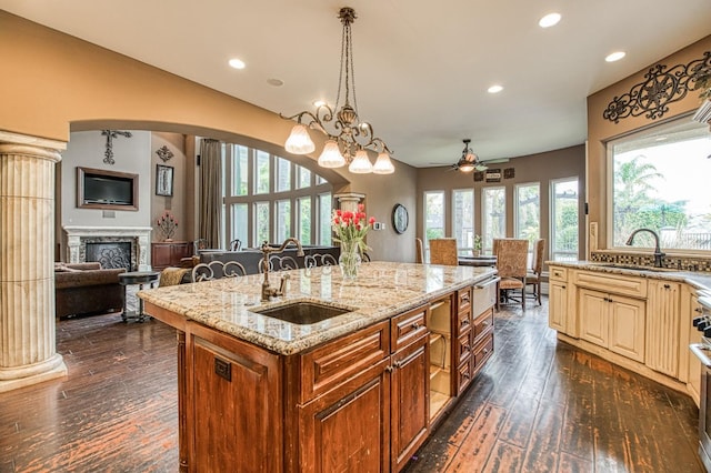 kitchen featuring cream cabinetry, a fireplace, open floor plan, a sink, and light stone countertops