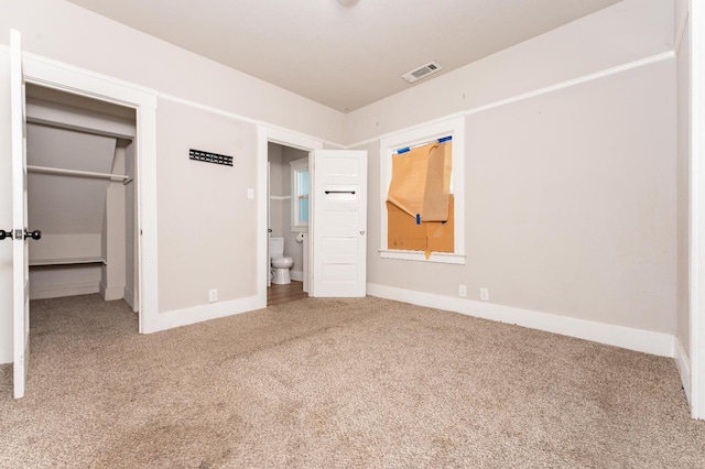 unfurnished bedroom featuring baseboards, visible vents, ensuite bath, a spacious closet, and carpet flooring