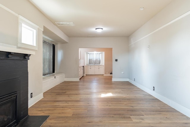 unfurnished living room with light wood-type flooring, a brick fireplace, visible vents, and baseboards