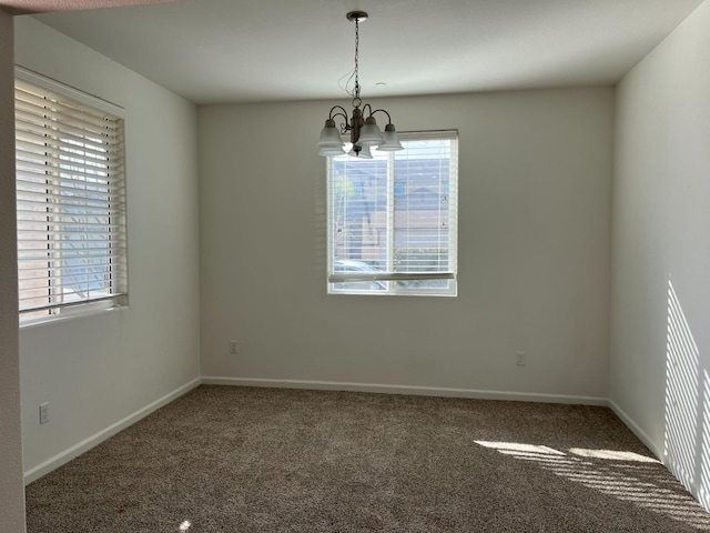 empty room featuring a chandelier, dark carpet, and baseboards