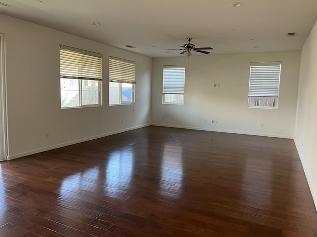 spare room with dark wood-style flooring, visible vents, ceiling fan, and baseboards