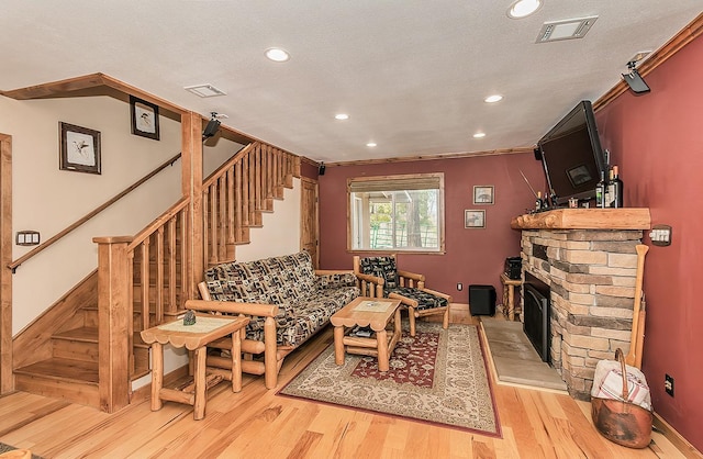 living area featuring a textured ceiling, visible vents, light wood-style floors, stairway, and a brick fireplace