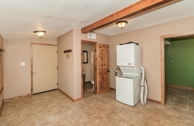 washroom with stacked washer and dryer, visible vents, a textured ceiling, laundry area, and baseboards