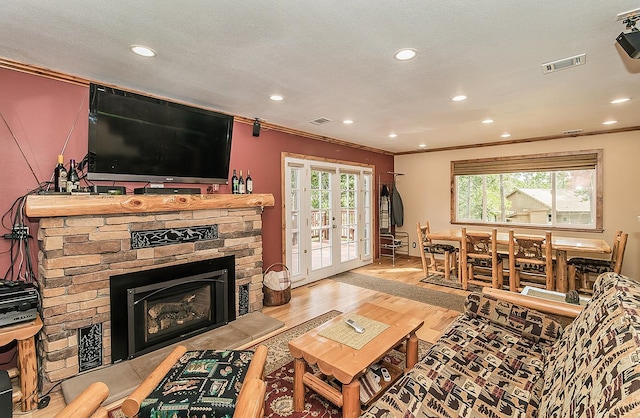 living room featuring crown molding, a fireplace, light wood finished floors, recessed lighting, and visible vents