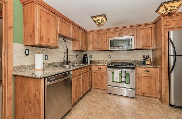 kitchen featuring stone counters, stainless steel appliances, a sink, brown cabinets, and decorative backsplash