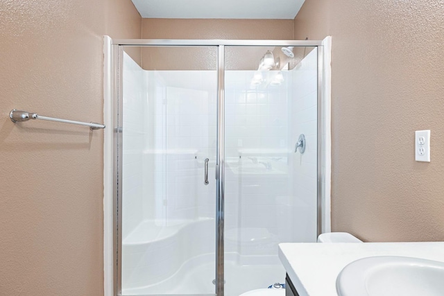 full bathroom with toilet, a stall shower, vanity, and a textured wall