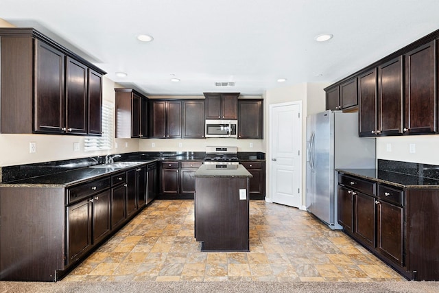 kitchen with a center island, visible vents, appliances with stainless steel finishes, dark brown cabinetry, and dark stone countertops