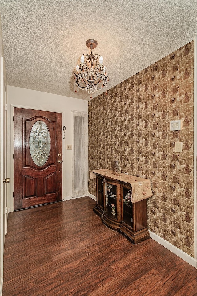 foyer entrance with dark wood-style floors, a textured ceiling, baseboards, and an inviting chandelier