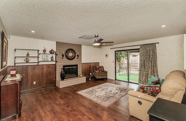 living room featuring dark wood-style flooring, visible vents, a brick fireplace, ceiling fan, and a textured ceiling