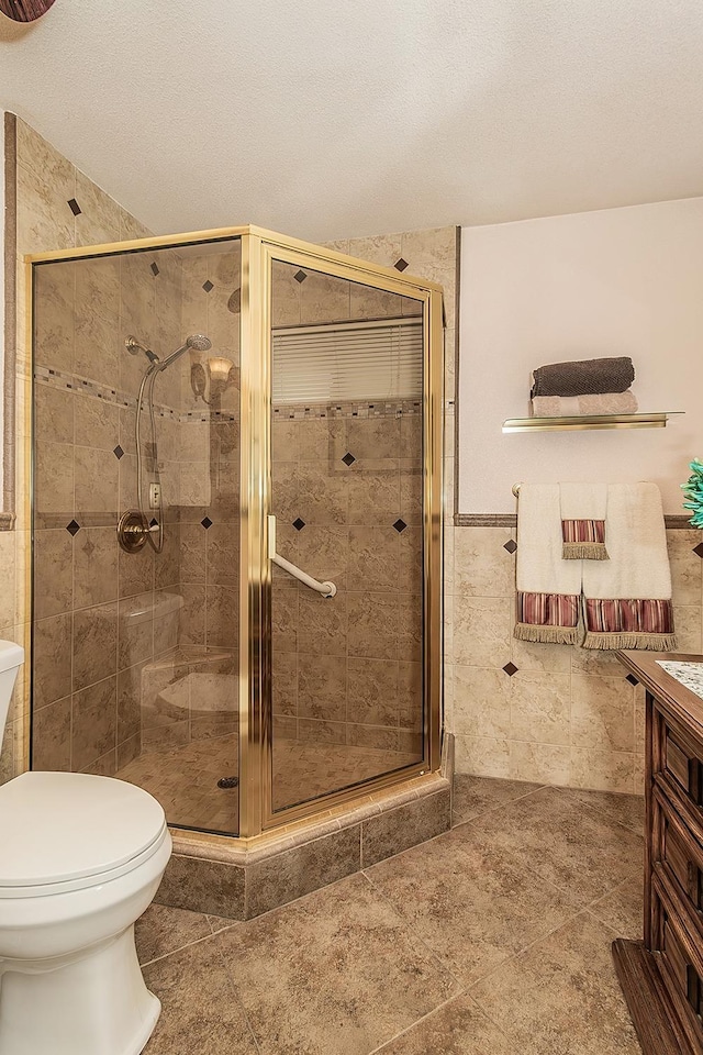 bathroom with a stall shower, toilet, a textured ceiling, vanity, and tile walls