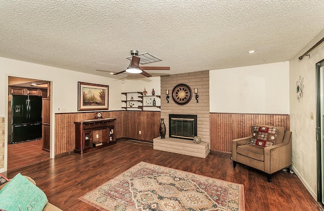 living room with a wainscoted wall, a fireplace, dark wood-style flooring, and a textured ceiling