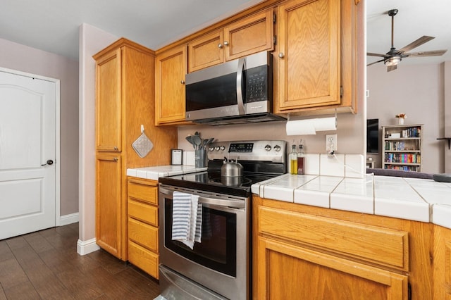 kitchen with dark wood finished floors, tile countertops, ceiling fan, appliances with stainless steel finishes, and brown cabinets