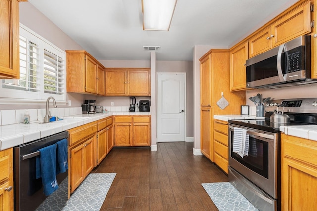 kitchen with tile countertops, visible vents, appliances with stainless steel finishes, brown cabinetry, and dark wood-type flooring