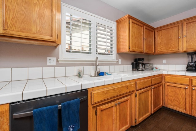 kitchen featuring brown cabinetry, dishwasher, tile countertops, dark wood-style floors, and a sink