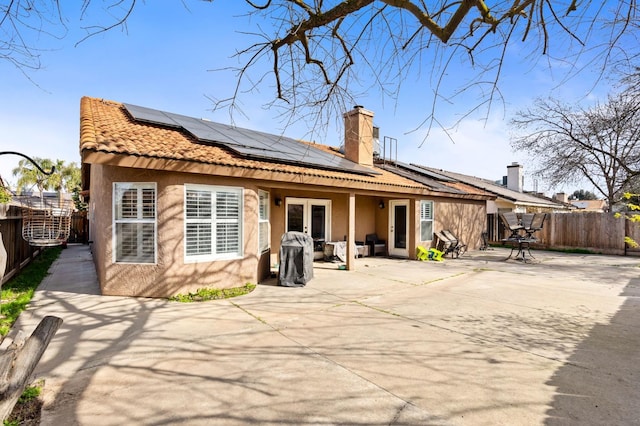 back of property featuring fence, french doors, roof mounted solar panels, stucco siding, and a patio area