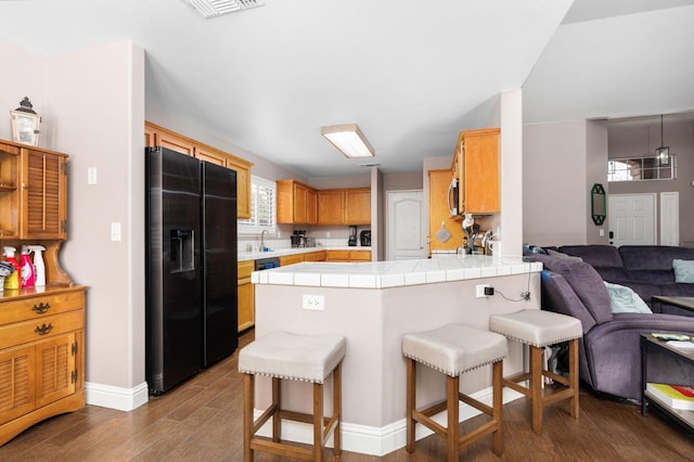 kitchen with black fridge with ice dispenser, tile countertops, open floor plan, dark wood-style flooring, and a peninsula