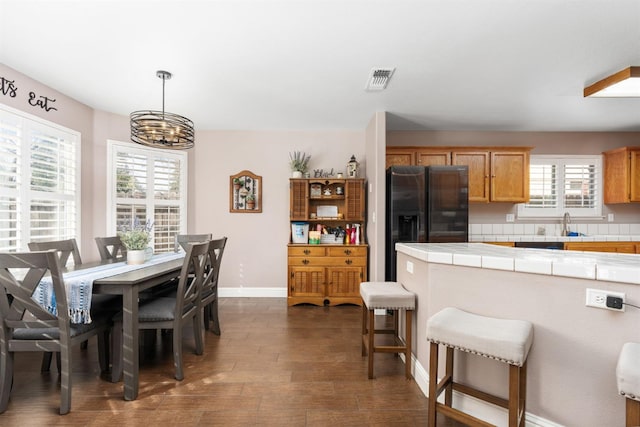 kitchen featuring dark wood-style flooring, decorative light fixtures, stainless steel refrigerator with ice dispenser, tile countertops, and baseboards