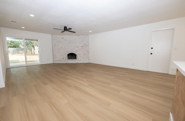 unfurnished living room featuring light wood finished floors, baseboards, visible vents, a ceiling fan, and a brick fireplace