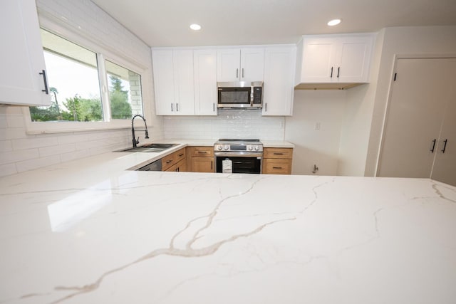 kitchen with white cabinets, appliances with stainless steel finishes, a sink, light stone countertops, and backsplash