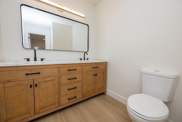 bathroom with double vanity, baseboards, toilet, wood finished floors, and a sink