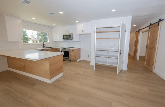 kitchen with a barn door, stainless steel appliances, a peninsula, white cabinets, and light countertops