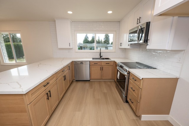 kitchen featuring appliances with stainless steel finishes, white cabinetry, a sink, light stone countertops, and a peninsula