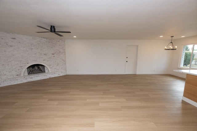 unfurnished living room with a fireplace, recessed lighting, light wood-style flooring, baseboards, and ceiling fan with notable chandelier